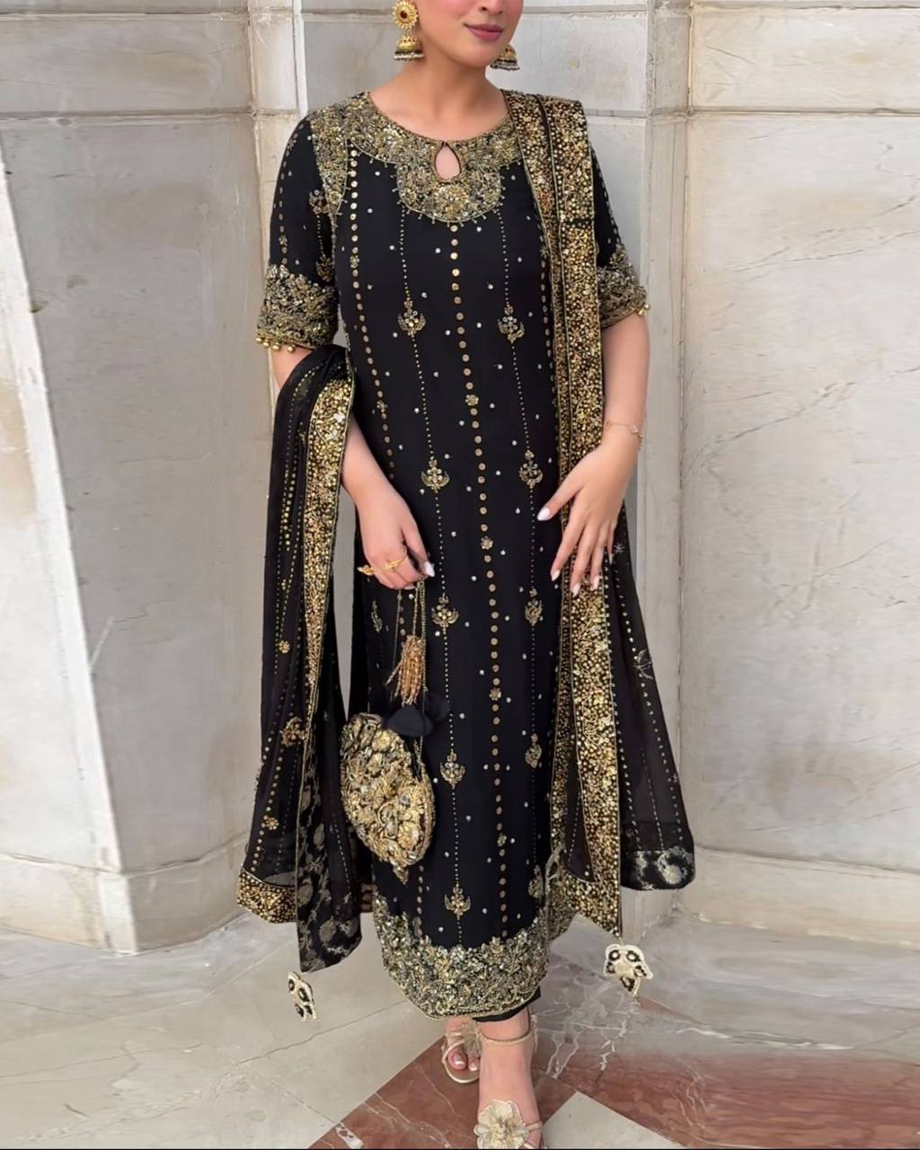 Woman wearing a black and gold embroidered traditional outfit with a matching dupatta.