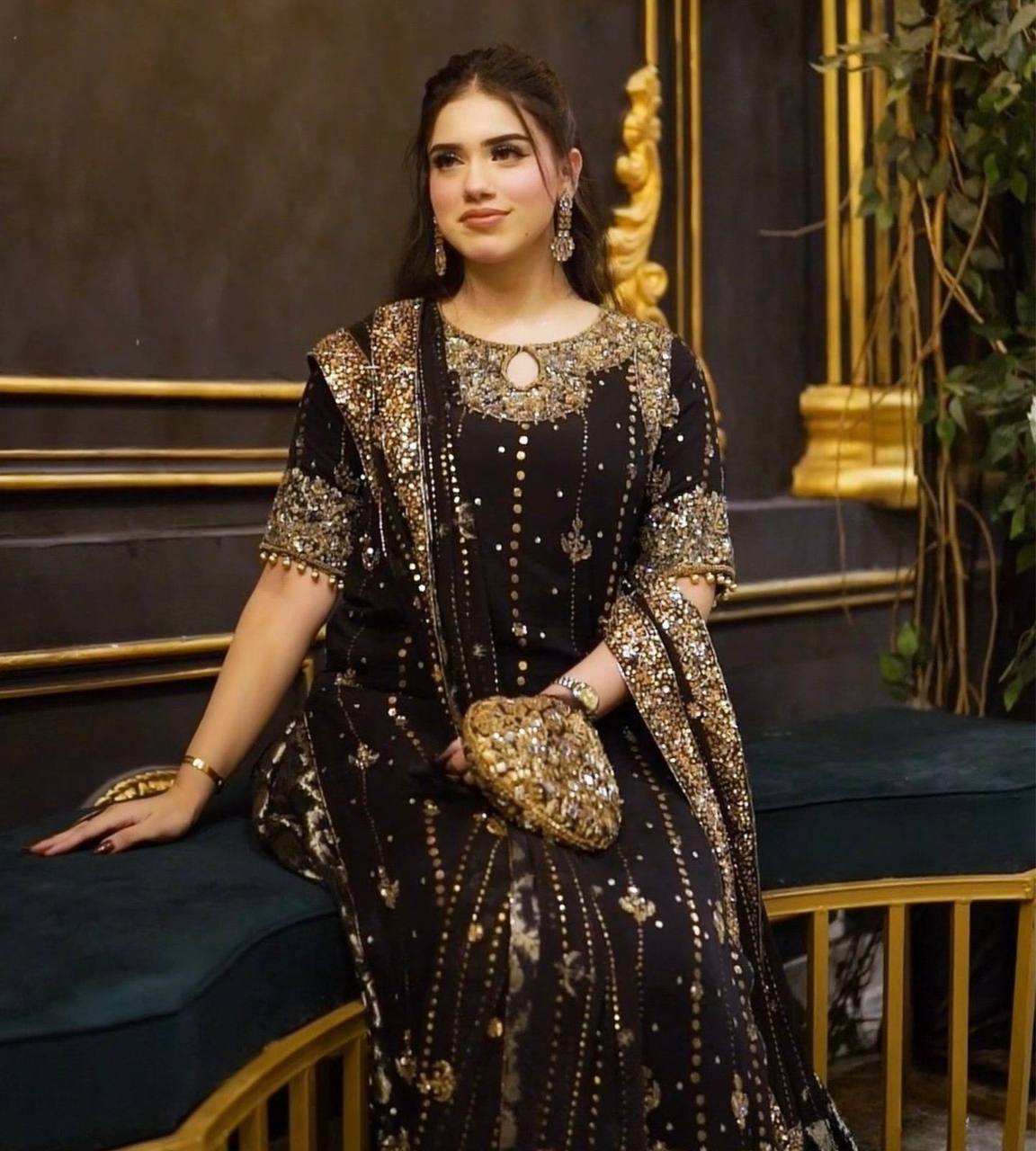 Woman in a black and gold dress sitting on a decorative chair.