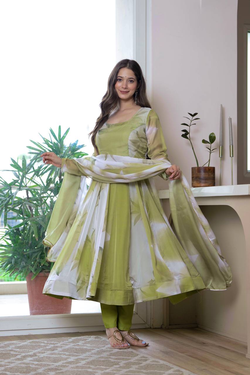 Woman in a green and white traditional outfit standing indoors with plants in the background