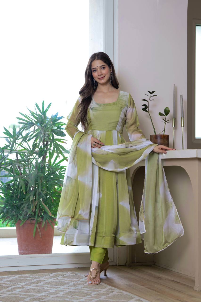 Woman in a green traditional outfit standing indoors with plants in the background