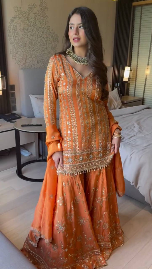 Woman in an orange traditional outfit standing in a bedroom.