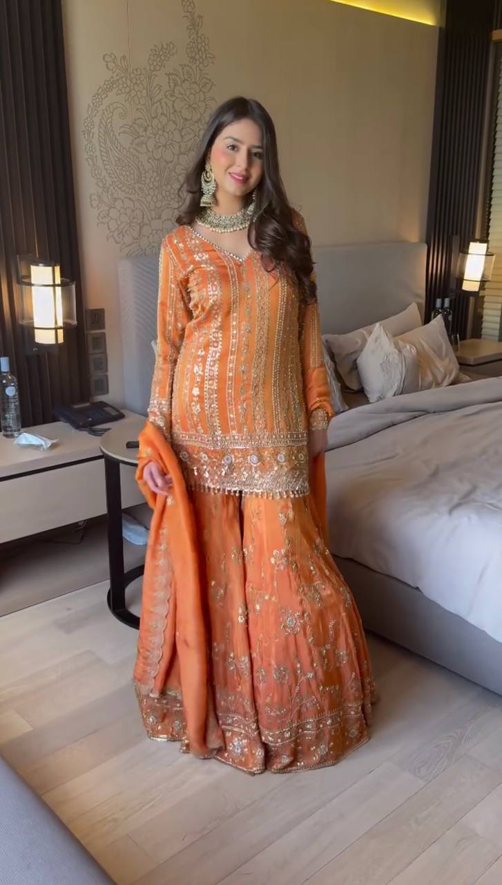 Woman in an orange traditional outfit standing in a bedroom.