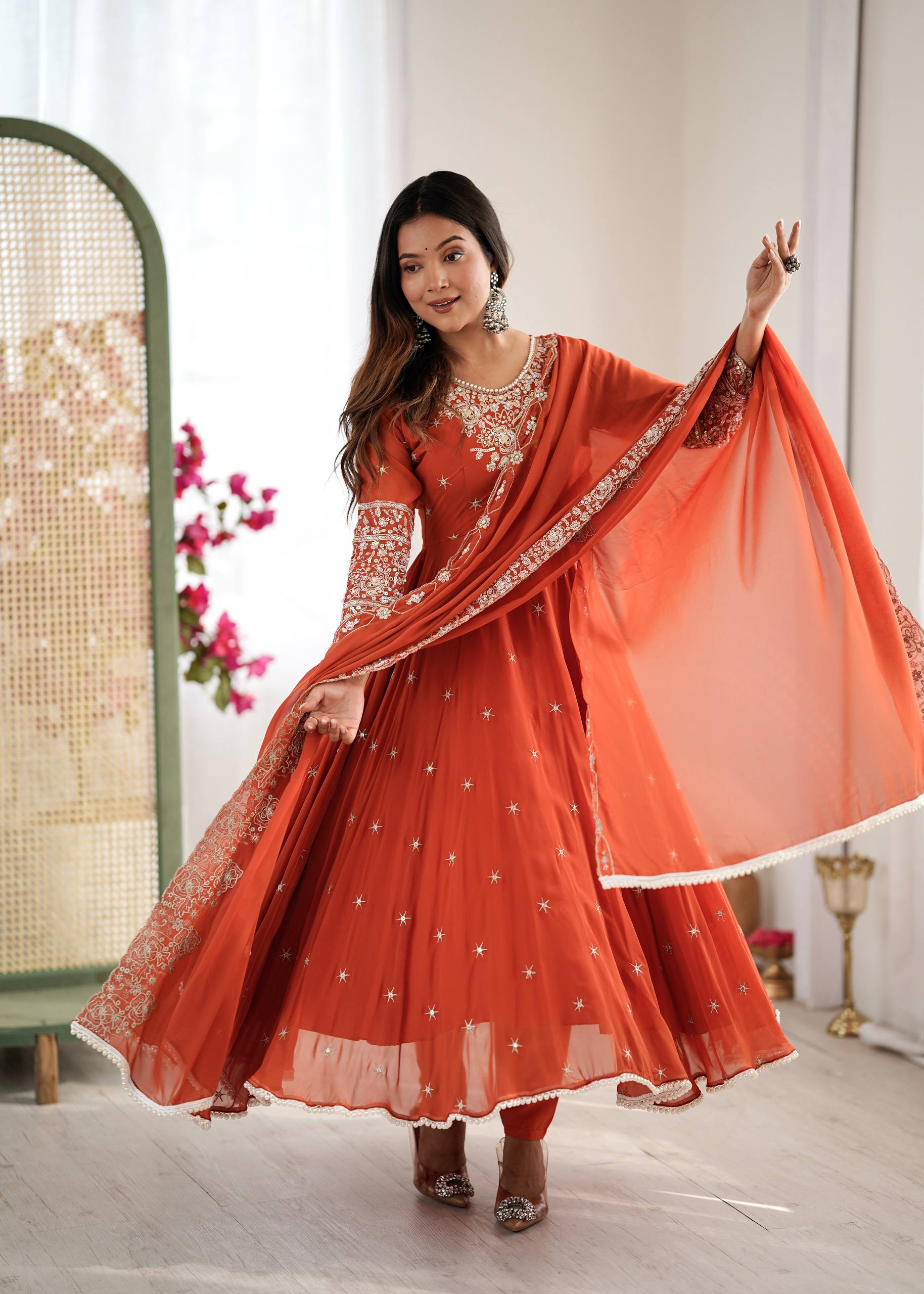 Woman in an orange traditional outfit with white embroidery in a bright room.
